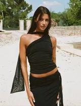 Top negro asimétrico con un solo hombro y detalle de tela transparente colgando del hombro.