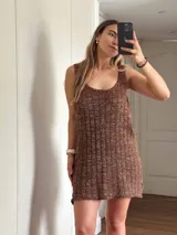 Vestido corto de tejido de punto color beige/dorado, con escote redondo y tirantes anchos. Presenta un tejido acanalado verticalmente con hilos de lurex que le dan brillo.