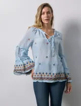 Blusa celeste de gasa bordada, con escote en V y lazo de ajuste. Mangas largas con terminación amplia.