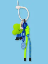 Llavero con un dije de peluche verde con forma de nube y piernas azules, un dije redondo azul con una cara sonriente, una cadena de eslabones azules y cordones trenzados de color azul y verde neón.