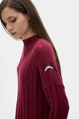 Sweater tejido color borgoña con cuello alto, corte oversize y mangas largas con detalle de trenzas verticales.