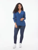 Blusa azul de corte amplio confeccionada en tejido de viscosa, con cuello en V, mangas largas con puños abotonados y aberturas laterales.