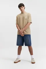 Remera beige de manga corta con textura y corte oversize. Presenta un pequeño bordado en relieve en el pecho.