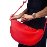 Cartera bandolera de cuero graneado color rojo, con forma de media luna y correa ajustable.