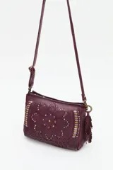 Cartera de cuero negro con diseño de flor mandala en relieve y apliques de tachas doradas y plateadas. Presenta flecos colgantes en uno de los laterales y correa ajustable para llevar al hombro o cruzada.