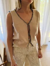 Chaleco tejido color arena con terminaciones en punto festón negro.