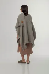 Ruana de punto color gris con diseño texturizado y terminación de flecos en el ruedo. Presenta un detalle de parche de cuero con logo en la parte frontal inferior.