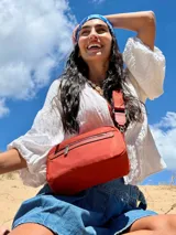 Bandolera color rosa viejo con detalles en cuero marrón claro, múltiples cremalleras metálicas y herrajes plateados. Incluye correa ancha ajustable con el logo de la marca.