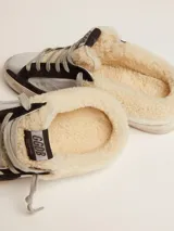 Zapatilla deportiva tipo mule, con cuerpo principal plateado metalizado y estrella lateral en negro. Presenta forro interior y borde de cuello en shearling color crema. La suela es de goma desgastada.