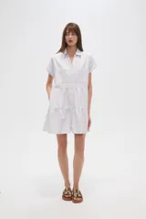 Vestido corto con cuello camisero, de corte holgado y mangas cortas. Presenta un diseño a rayas verticales en tonos beige y blanco, con volados en la falda y cierre frontal con botones.