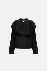 Blusa negra de viscosa con cuello perkins y manga larga. Detalles de bordados, lentejuelas y volantes. Cierre en la espalda con abertura y botones.