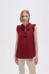 Blusa sin mangas color borgoña con cuello alto con volantes y lazo.