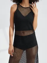 Vestido largo negro de malla con escote redondo y tirantes finos. El vestido es transparente y se lleva sobre un conjunto de ropa interior o traje de baño negro.