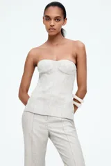 Top bustier de sarga color crudo, con escote strapless, copas acolchadas y costuras decorativas adelante y atrás. Tiene varillas delanteras para dar forma y aportar sujeción, y cierre visible en la espalda. Está forrado.