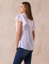 Blusa blanca de gasa con broderie, cuello a la base, escote en V y lazo de ajuste. Delantera broderie con corte y frunces. Manga corta volado de broderie. Espalda con corte y frunces.