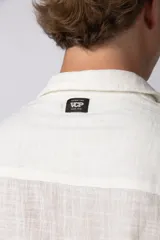 Camisa de lino color blanco, de manga corta, con cuello clásico y cierre frontal con botones.