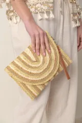 Sobre de mano tipo clutch confeccionado en rafia color beige con detalles de lurex dorado.