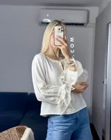 Blusa blanca de mangas largas con volados en los puños y escote con lazo.