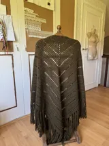 Ruana tejida a mano en color lila, confeccionada en lana merino. Presenta un diseño de punto con calados diagonales y terminación de flecos largos en el ruedo.