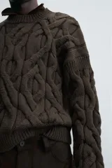 Sweater marrón oscuro de punto con estructura de trenzas, cuello redondo, manga larga y corte regular fit.