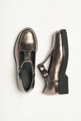 Zapato guillermina color bronce con acabado metalizado, con correa sobre el empeine con hebilla ajustable y suela de goma negra con plataforma.