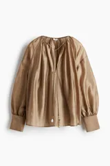 Blusa color dorado de lyocell con cuello redondo con cordón ajustable, abertura en V y mangas globo largas con puños vueltos con abertura y botón.