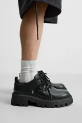Zapato tipo derby de cuero negro con cordones y ganchos metálicos. Suela track con plataforma.