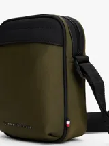 Cartera tipo reporter Tommy Hilfiger color verde militar con detalles en negro. Presenta correa ajustable, bolsillo frontal con cierre y logo metálico de la marca.
