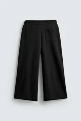 Pantalón jogger negro de corte relaxed fit, confeccionado en tejido de algodón. Presenta cintura elástica ajustable con cordón, pliegues frontales, bolsillos delanteros y un bolsillo trasero.