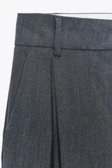Pantalón marrón de tiro alto con trabillas, doble pliegue, bolsillos laterales y de vivo en la espalda, pernera ancha y cierre frontal con cremallera y gancho metálico.