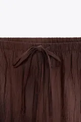 Falda midi color ocre de tejido arrugado con cintura elástica ajustable con cordones y bolsillos laterales ocultos en la costura.