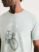 Camiseta blanca de algodón con cuello redondo y mangas cortas. Estampa rectangular con borde negro que contiene la frase "NATURAL ATMOSPHERE" en letras mayúsculas y una imagen de montañas y mar.