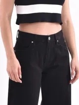 Pantalón de jean negro, tiro alto, de corte ancho (wide leg) y largo hasta el tobillo. Presenta cierre frontal con botón y bolsillos clásicos de jean.