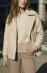 Campera de abrigo color crema, con cuello solapa y cierre frontal asimétrico. Presenta textura bouclé o de lana rizada.