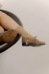 Mocasín de cuero color marrón con tachas metálicas plateadas en la puntera y laterales.