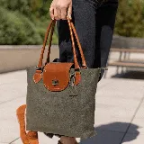 Cartera tipo tote de cuero vacuno color verde oliva con solapa de cuero marrón y herrajes plateados. Tiene doble asa de cuero marrón, bolsillo interno con cierre y cierre principal con cremallera.