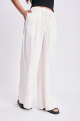 Pantalón de lino blanco de corte amplio, con cintura alta y lazo marrón con flecos.