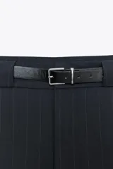 Falda pantalón corta color azul marino a rayas verticales, de tiro medio con cinturón negro de hebilla metálica. Cuenta con bolsillos laterales y cierre frontal con cremallera y gancho metálico.