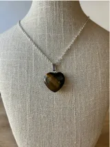 Collar con cadena plateada y dije de piedra natural ojo de tigre tallada en forma de corazón.