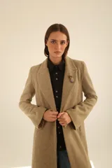 Tapado largo color beige con solapas de muesca, cierre frontal con botones y un prendedor de flores en la solapa.