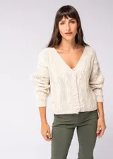 Saco color beige de tejido de punto trenzado, con escote en V y cierre frontal con botones marrones.
