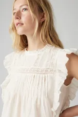 Blusa blanca sin mangas con cuello alto y detalles de encaje y volados.