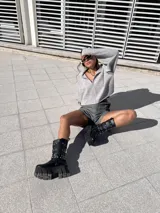 Bota negra de ecocuero con caña media, plataforma track y tres correas con hebillas plateadas.