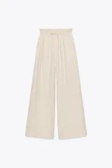 Pantalón palazzo color crudo, confeccionado en tejido fluido con mezcla de lyocell. Presenta tiro medio, cintura elástica ajustable con cordones, bolsillos laterales ocultos en costura y pierna ancha.