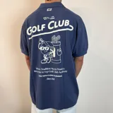 Chomba color beige con cuello clásico, corte oversize, mangas cortas y bordados marrones con la inscripción "Golf Club" y otros motivos. 