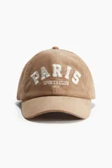Gorra de béisbol color beige confeccionada en pana de algodón. Presenta bordado frontal con la leyenda "Paris Sports Club 1972" en color blanco.