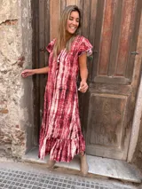 Vestido largo de seda con estampado tie-dye en tonos rojo y blanco, con mangas cortas con volados y ruedo con volados.