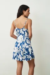 Vestido corto de color negro con tirantes finos y escote en V. Presenta un detalle fruncido en el pecho, cintura elastizada y falda con un volante en el bajo.