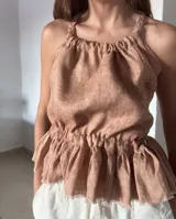 Blusa color ladrillo confeccionada en lino, con tiras trenzadas regulables que se cruzan en la espalda y elástico en la cintura.