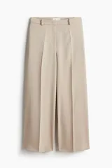 Pantalón de vestir color beige, de corte amplio y largo tobillero, con pliegues delanteros y traseros, bolsillos laterales y traseros decorativos. Cierre con corchete y botón oculto.